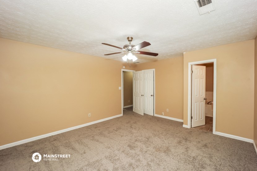 an empty living room with a ceiling fan and a door to a bathroom