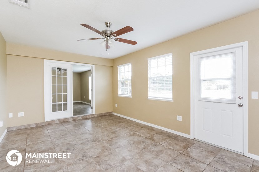 an empty living room with a ceiling fan and a door to a hallway