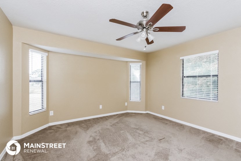 an empty living room with a ceiling fan and two windows