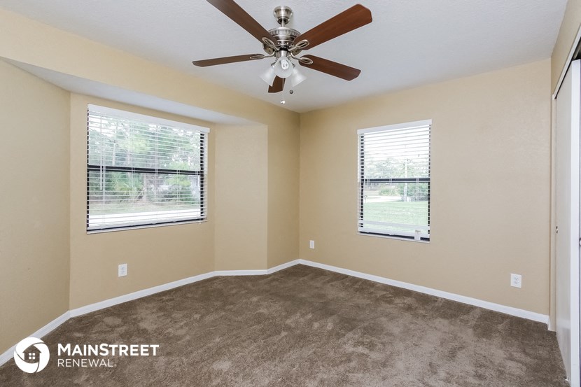an empty room with a ceiling fan and two windows