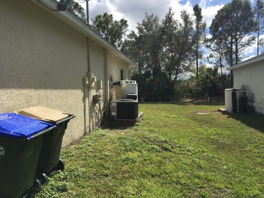 the side of a house with a yard and some trash cans