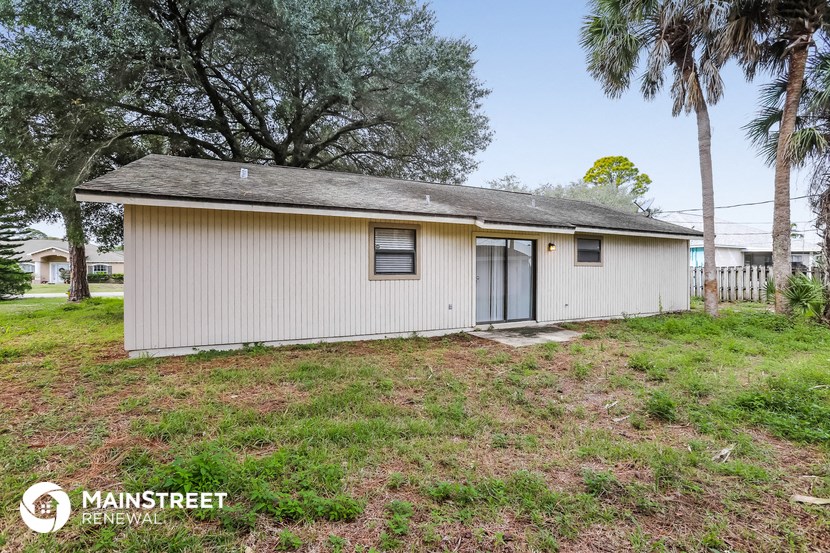 a small white house with a yard and palm trees