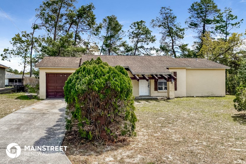 a small white house with a garage and a tree in the yard