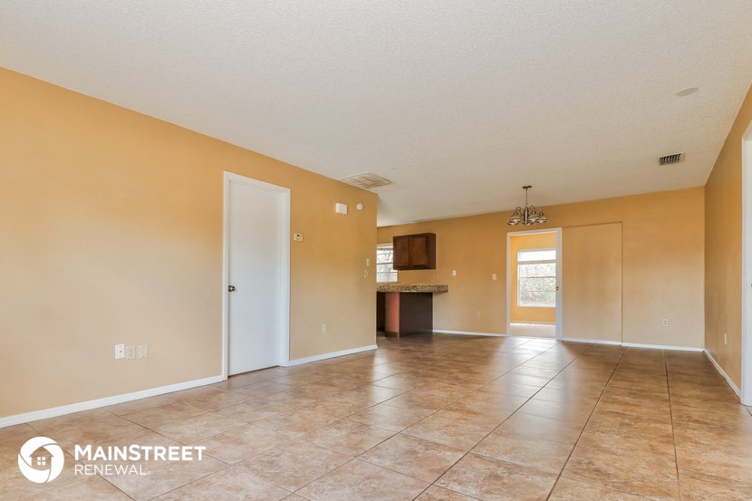 a spacious living room with tile flooring and a kitchen