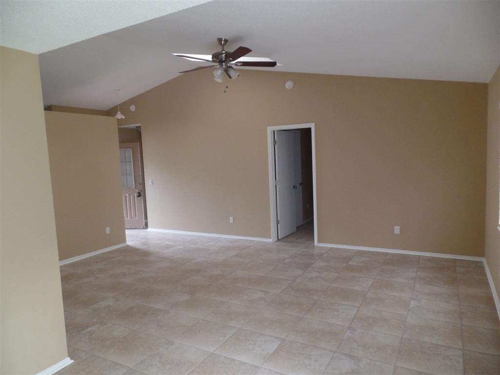 an empty living room with a ceiling fan and tile floor