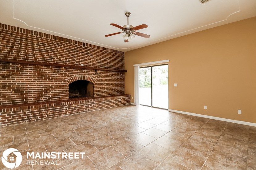 a empty living room with a brick fireplace and a ceiling fan