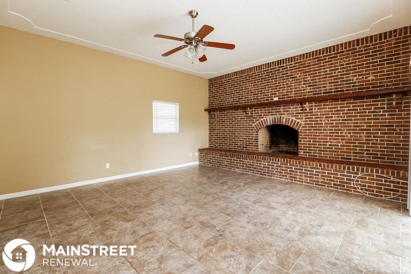 a living room with a brick fireplace and a ceiling fan