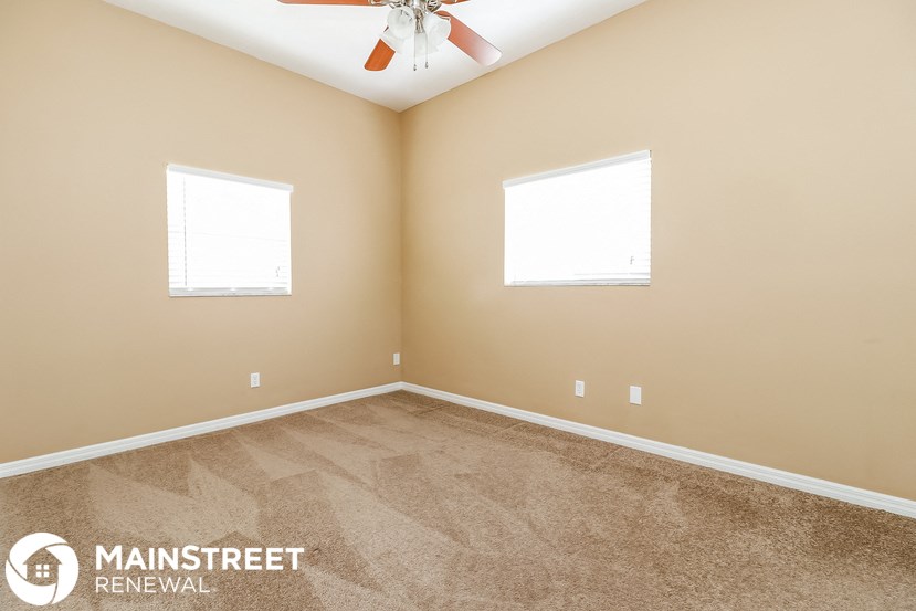 a bedroom with carpet and two windows and a ceiling fan