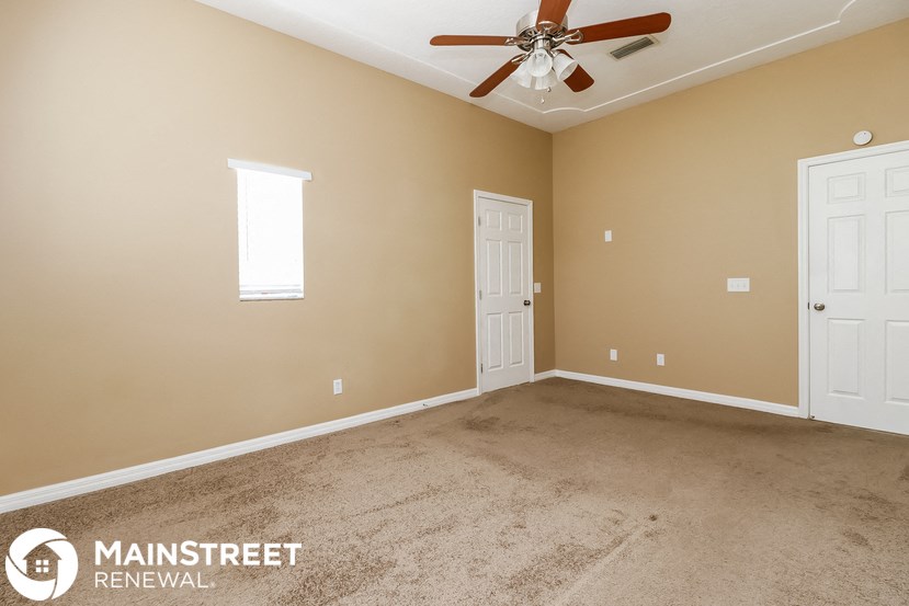a carpeted living room with a ceiling fan and two doors