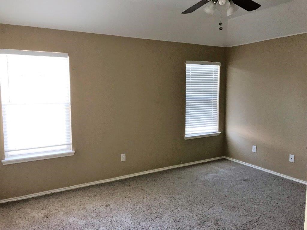 an empty room with a ceiling fan and two windows