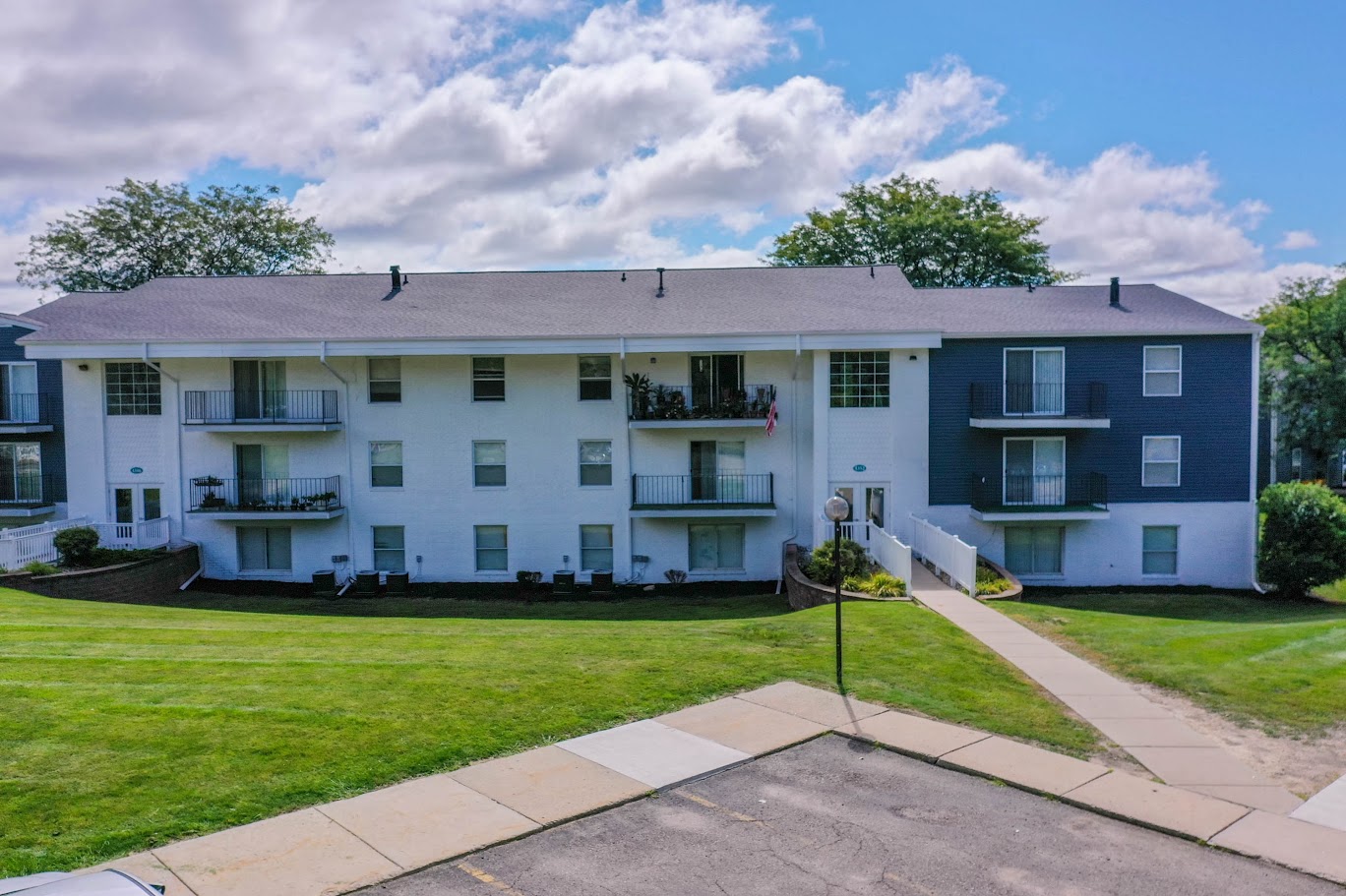 a white apartment building with a green lawn and blue sky