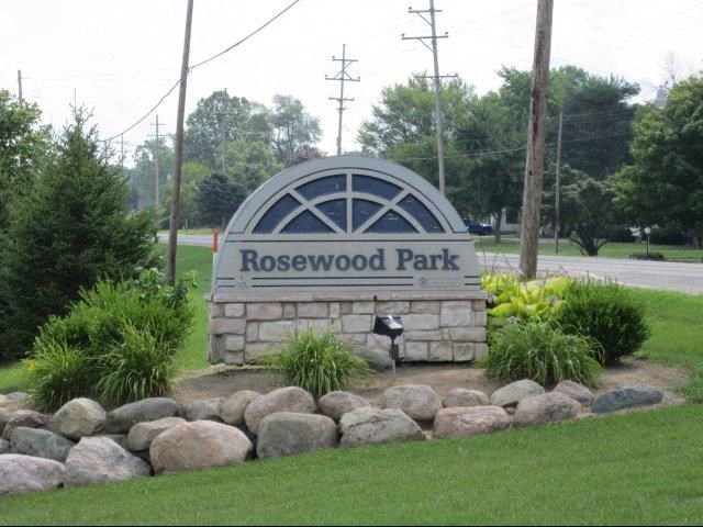 the rosewood park sign is in front of the grass and rocks