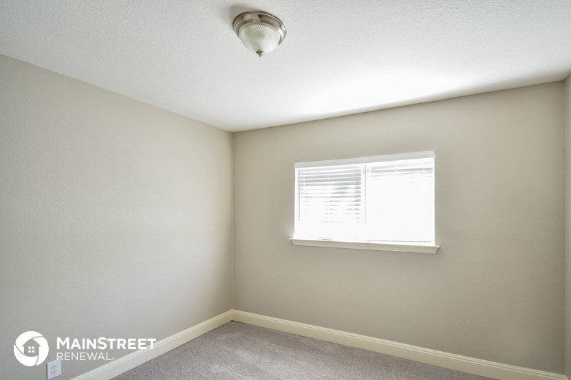 the bedroom of an apartment with a window and a ceiling fan