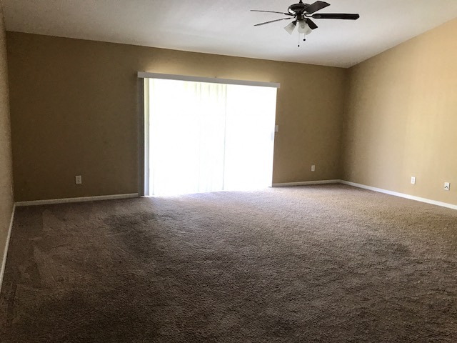 an empty living room with a ceiling fan and a window