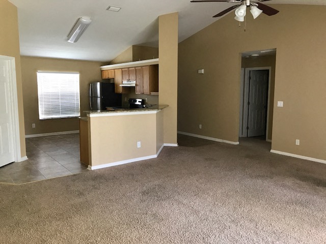 an empty living room with a kitchen and a ceiling fan