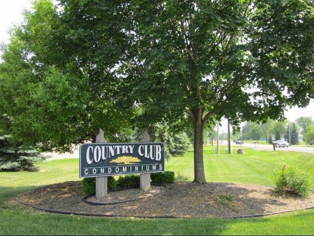 a sign for the country club condominiums under a tree