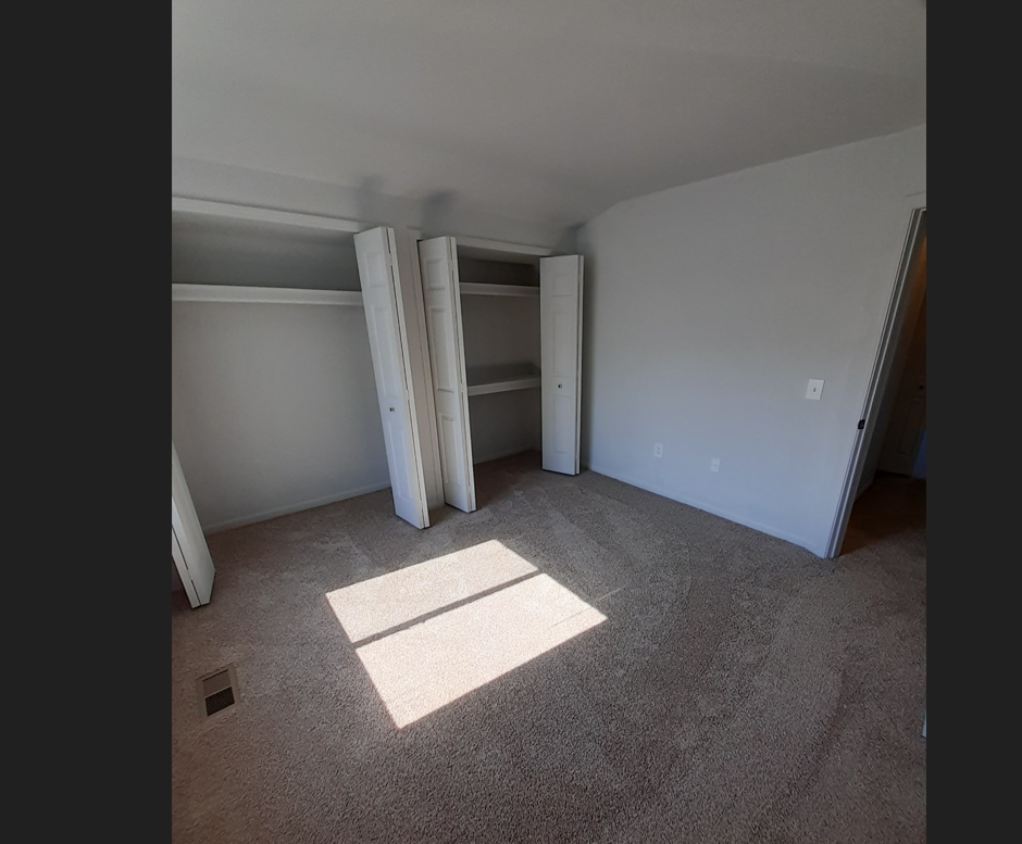 a room with a carpeted floor and three open closet doors