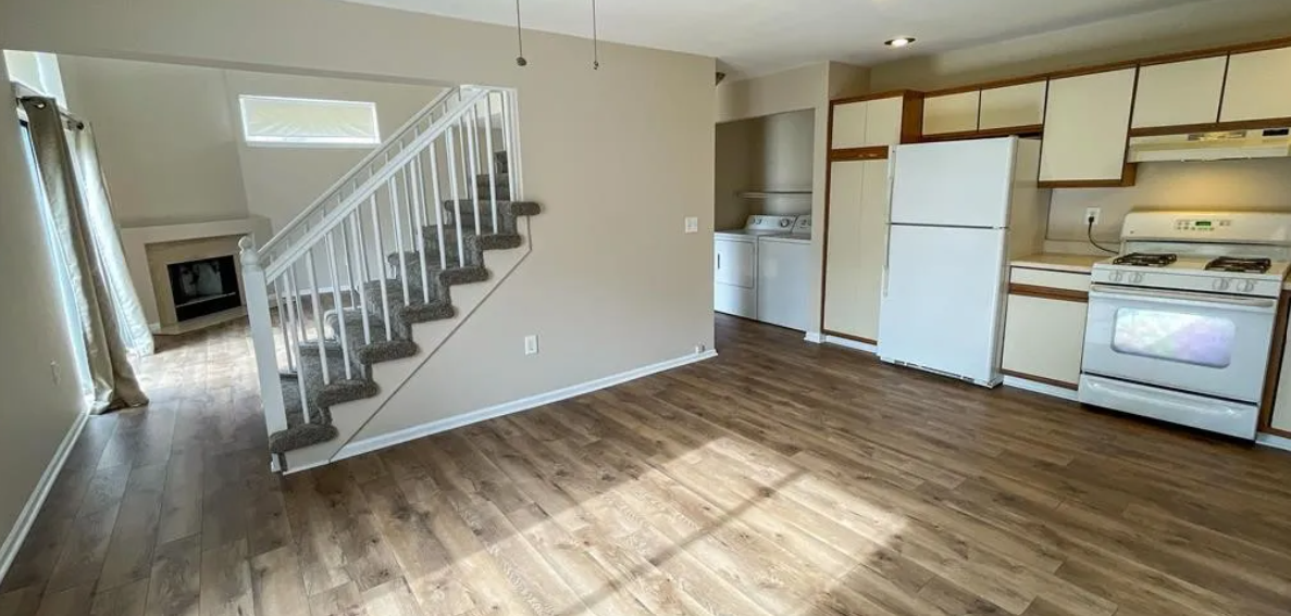 an empty living room with a staircase and a kitchen
