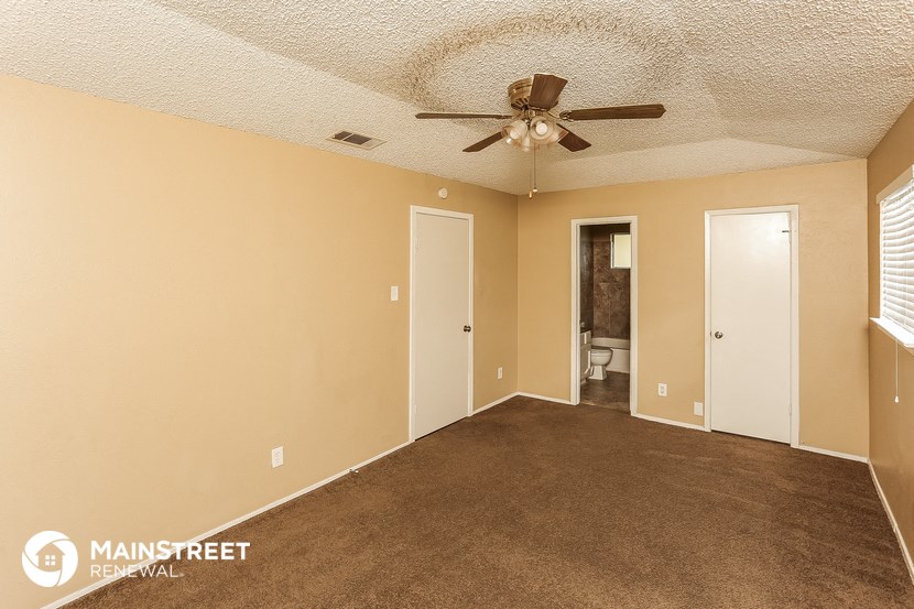a carpeted living room with a ceiling fan and a door to a bathroom