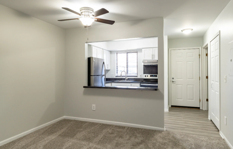 an empty living room with a ceiling fan and a kitchen