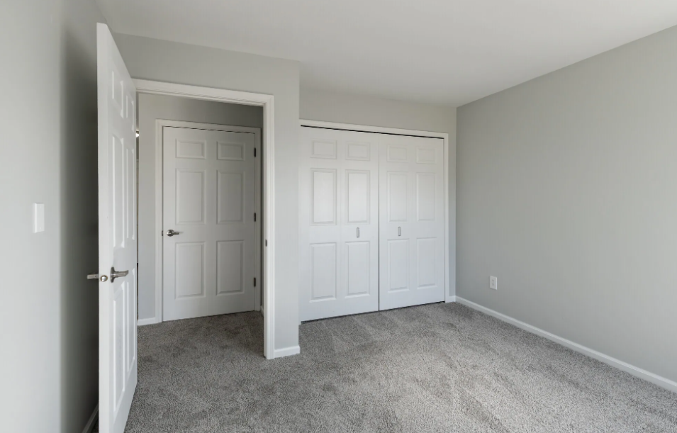 a bedroom with white doors and carpeting and a door to a closet