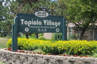 a sign that says tapiola village with yellow flowers in front of it