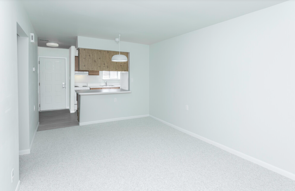 an empty living room with a kitchen in the background