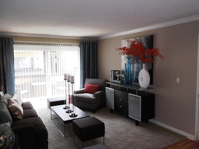 A living room with a black couch, a grey armchair, a black coffee table, and a black cabinet with a vase of red flowers on top.