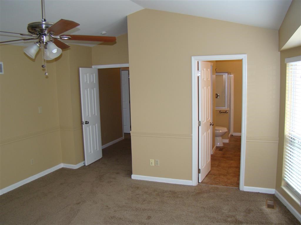 an empty living room with a ceiling fan and a door to a bathroom