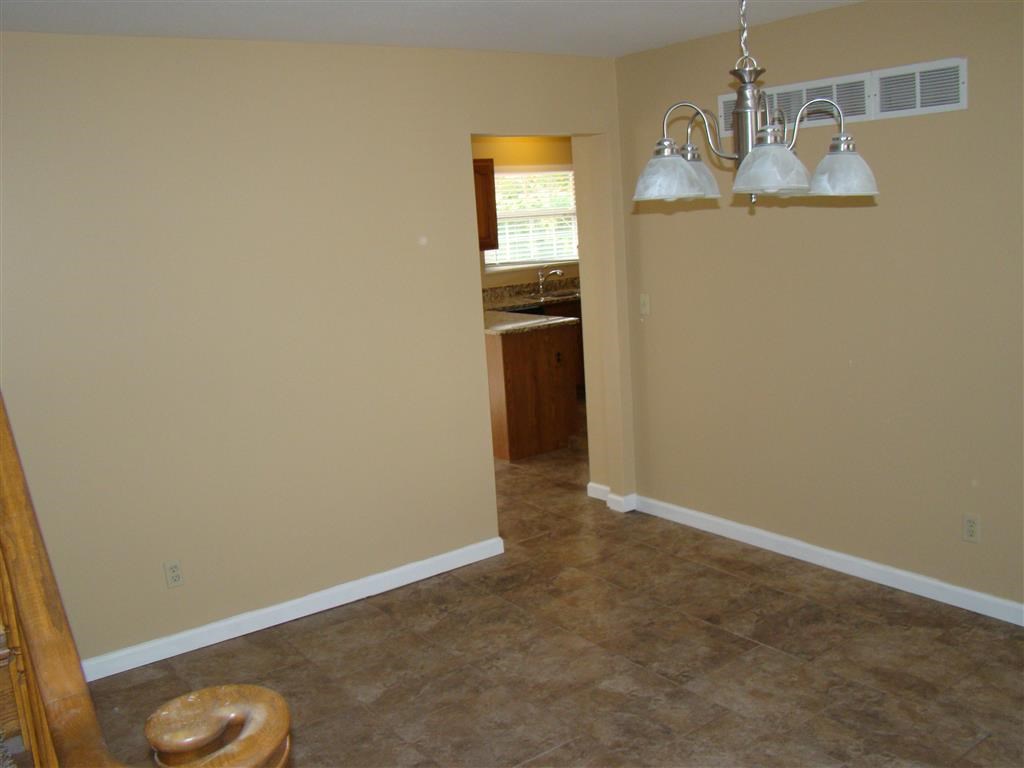 an empty living room with a chandelier and a kitchen