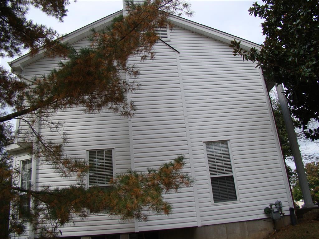 the side of a white house with a tree in front of it