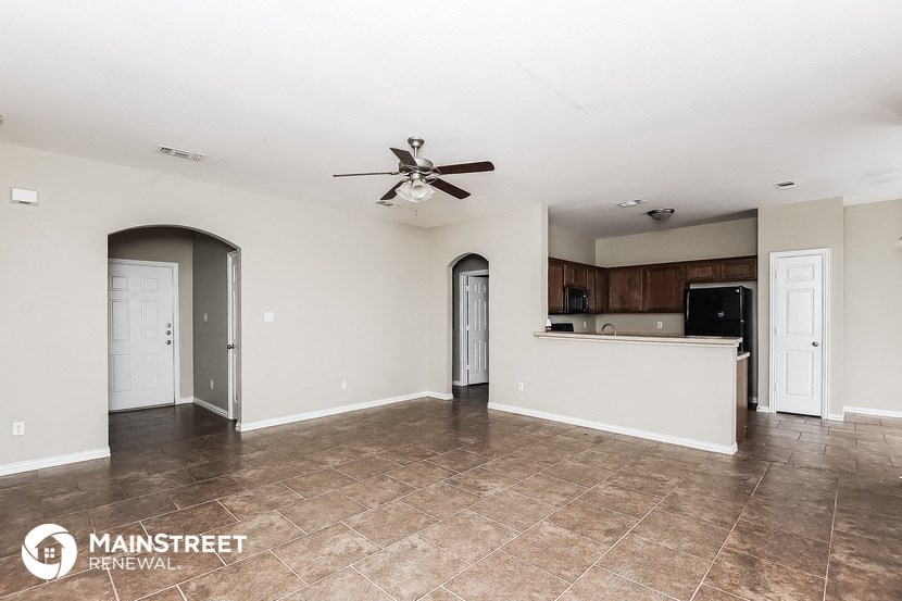 an empty living room with a kitchen and a ceiling fan