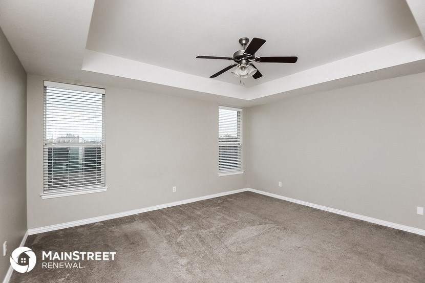 an empty living room with a ceiling fan and two windows