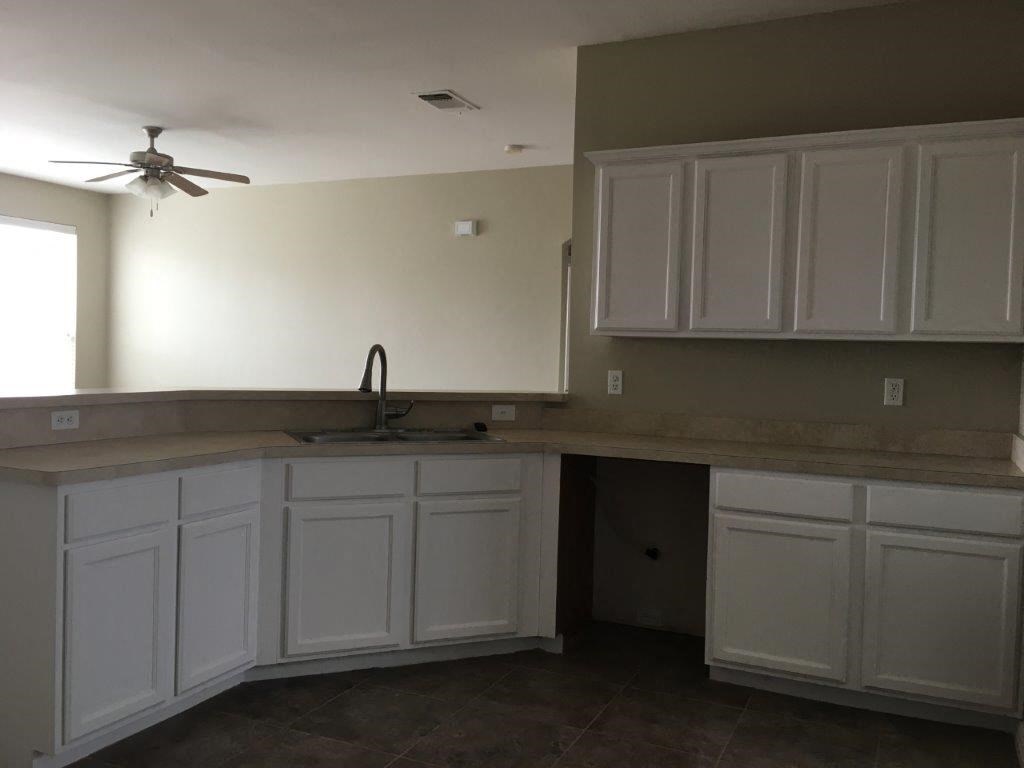 an empty kitchen with white cabinets and a ceiling fan
