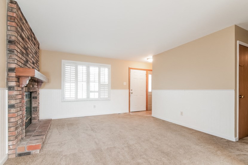 an empty living room with a brick fireplace and white walls