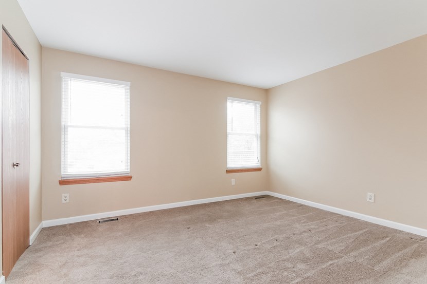 an empty room with two windows and a carpet