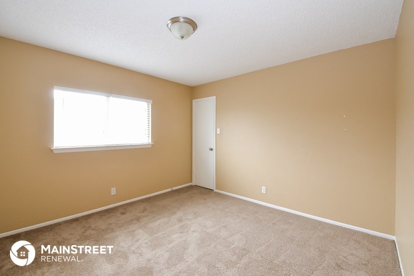 the spacious bedroom with carpeted flooring and a window