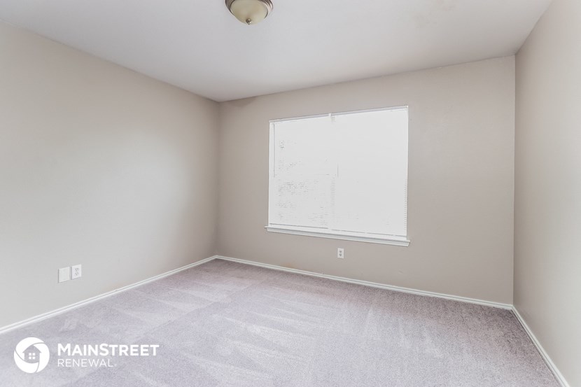 the bedroom of an apartment with white carpet and a window