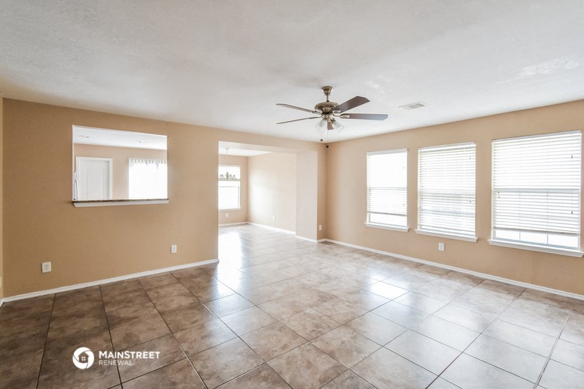 an empty living room with a ceiling fan and windows