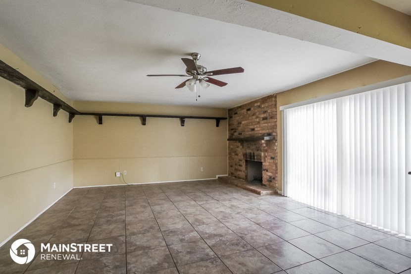 an empty living room with a ceiling fan and a brick fireplace