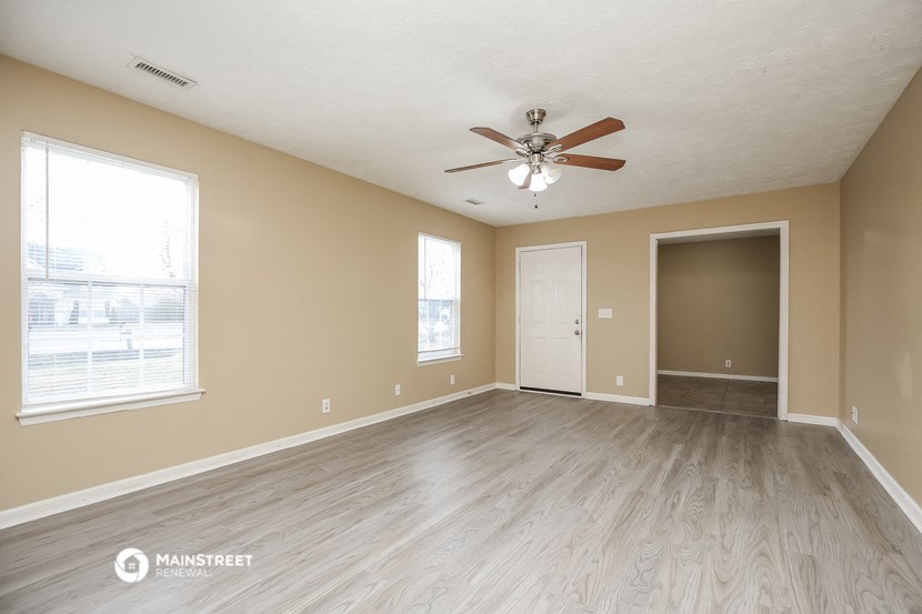 the spacious living room with wood flooring and a ceiling fan