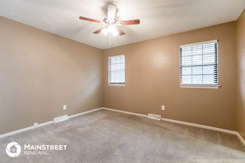 an empty room with a ceiling fan and two windows
