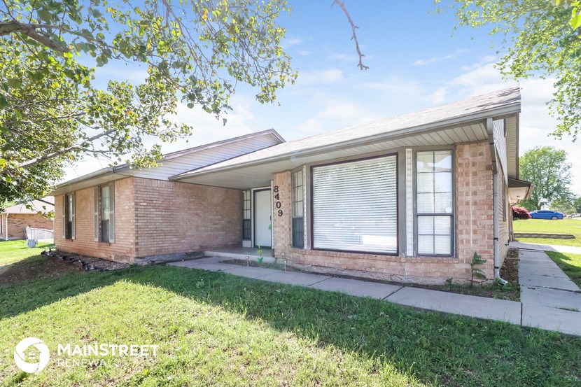 the front of a brick house with a sidewalk and grass
