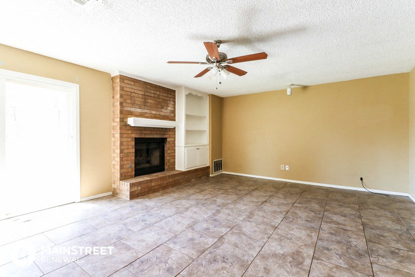 an empty living room with a brick fireplace and a ceiling fan