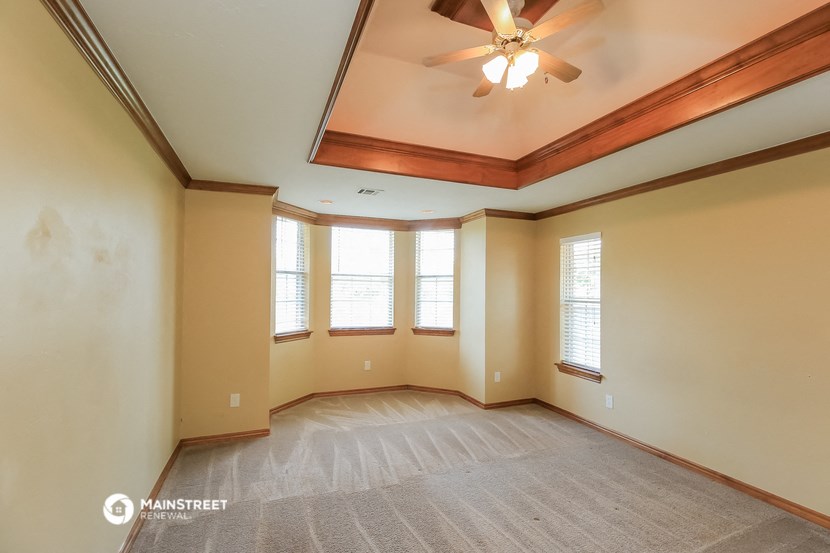 an empty living room with a ceiling fan and three windows