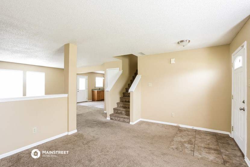 the living room and dining room of a manufactured home with carpet and a staircase