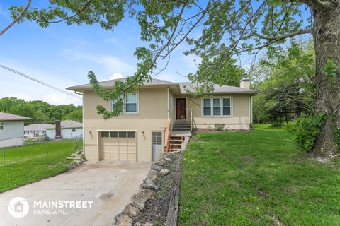 a beige house with a driveway and a tree