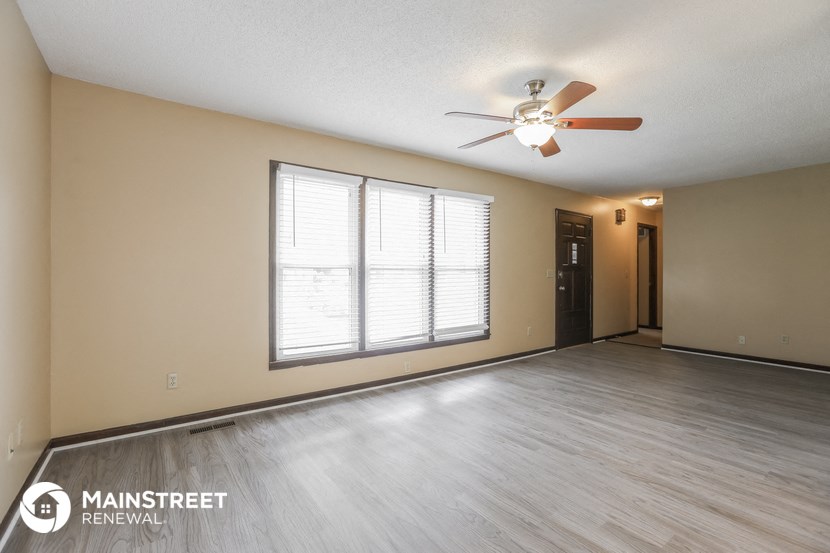 the spacious living room with a ceiling fan and a large window