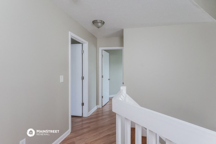 a bedroom with white walls and a hallway with doors and a staircase