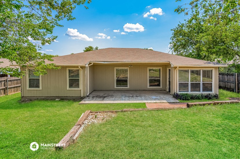 a small tan house with a grassy yard and trees